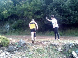 Two participants running on a dirt road during the Skiathos Trail Run 2018 while a man points at them.